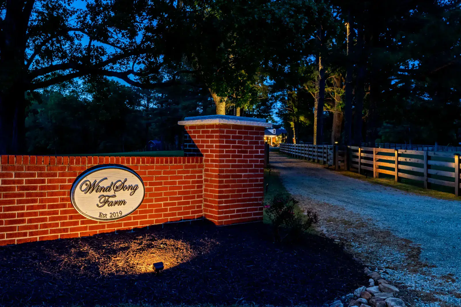 Commercial outdoor lighting illuminating the WindSong Farm brick entrance sign and tree-lined driveway at night in Middle Tennessee by Light TN