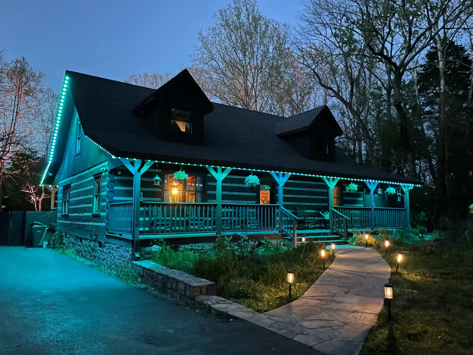 Permanent roofline lighting on a log cabin with teal LED soffit lights and path lighting at dusk in Middle Tennessee by Light TN