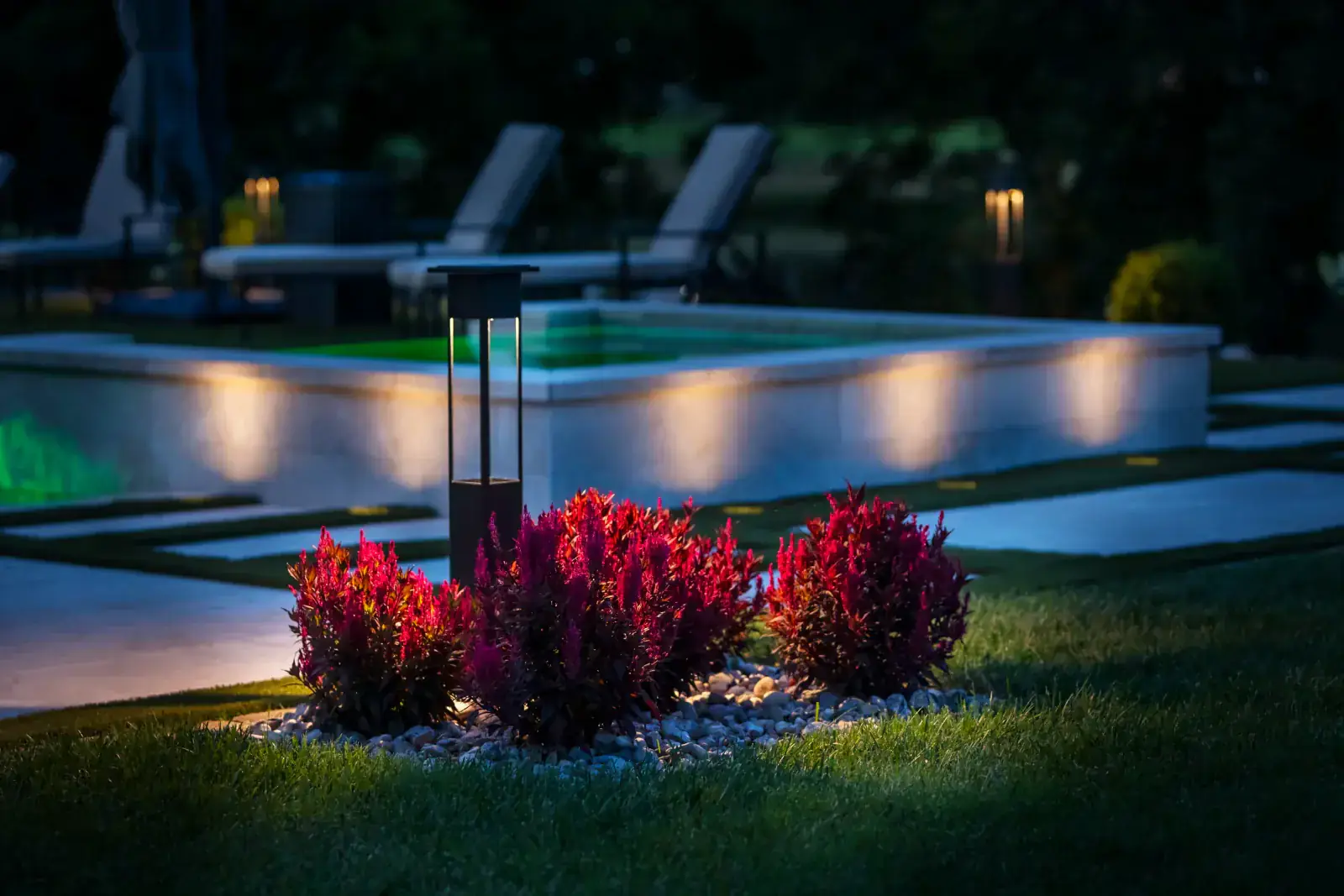 Outdoor lighting installation showing a bollard path light beside red flowering shrubs with pool surround lighting at night in Middle Tennessee by Light TN
