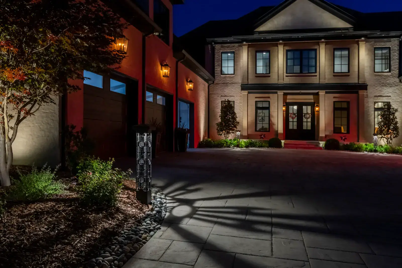 A luxury home driveway lit in layers at night with architectural and landscape lighting